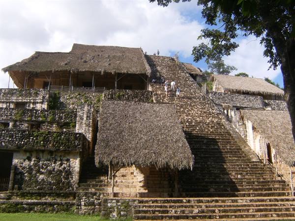 Tourists climb the stone staircase of Ek Balam acropolis with thatched roofs