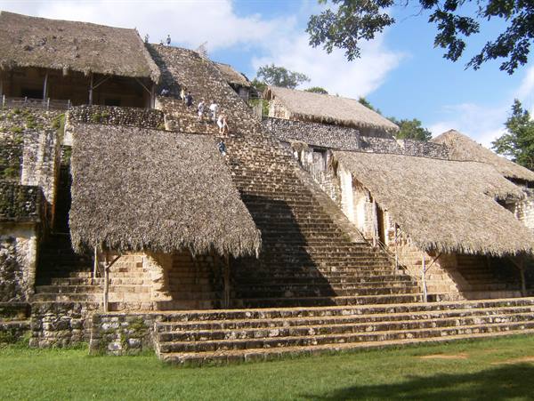 Tourists climb the stone staircase shaded by thatched roofs, Ek Balam