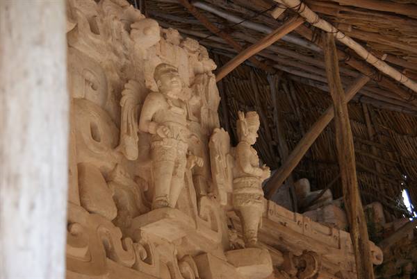 Maya stucco figures carved in stone under thatched roof shelter