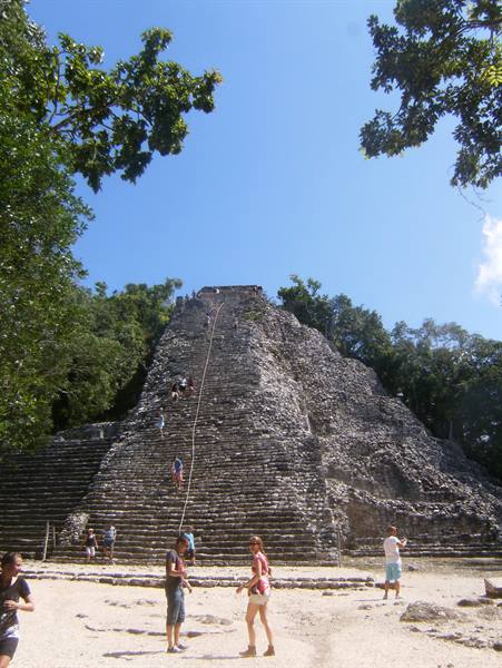 Tourists climb the great stone pyramid at Cobá under sunny skies