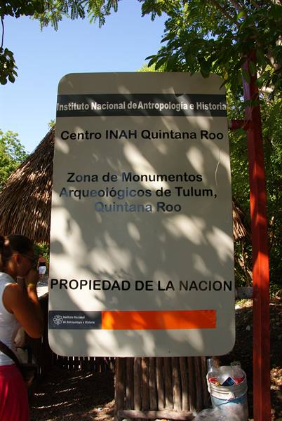 INAH sign at the Tulum archaeological zone entrance, amid trees and shade