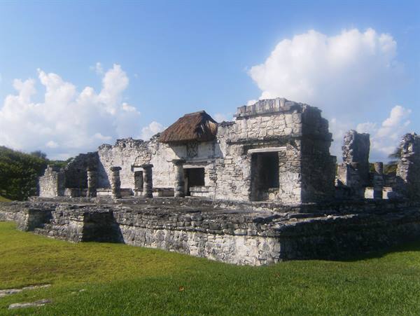 Mayan stone ruins with thatched roof at Tulum, grassy lawn and cloudy sky
