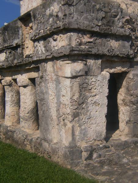 Carved stone face on Mayan temple with columns and grass