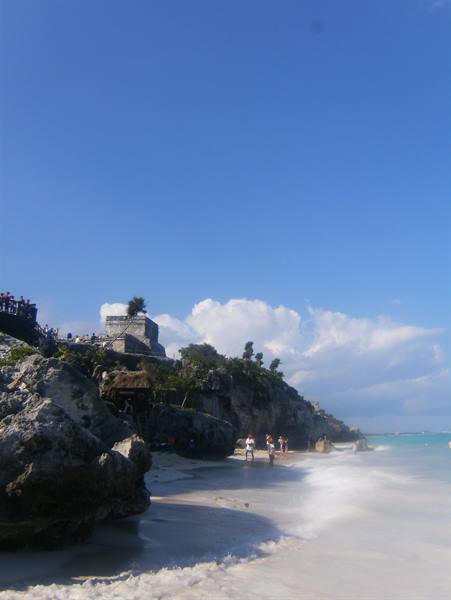 Tourists on the beach beneath Tulum's Mayan ruins, blue sky