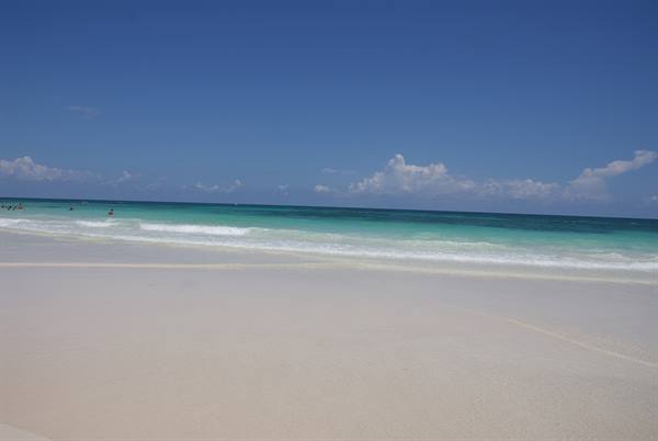 White sand beach with turquoise waves and swimmers under a blue sky