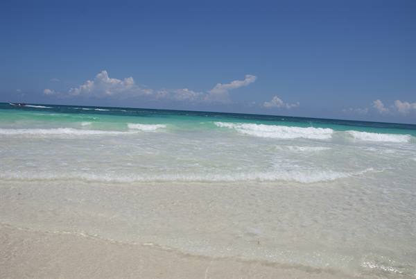 Turquoise waves on white sand beneath a blue sky with clouds