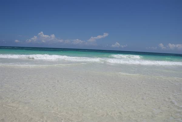 White waves breaking on pale sand, turquoise sea under blue sky