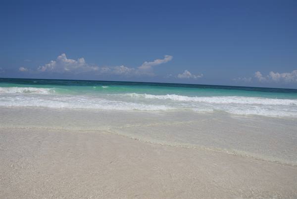 White waves breaking on pale sand under blue sky with clouds