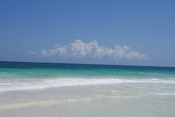 White waves on pale sand, turquoise sea and clouds on the horizon