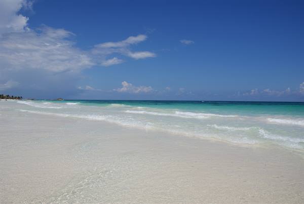 Gentle turquoise waves wash over white sand under a blue sky
