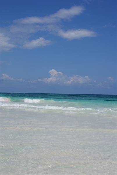 White sand beach with turquoise waves and cloudy blue sky