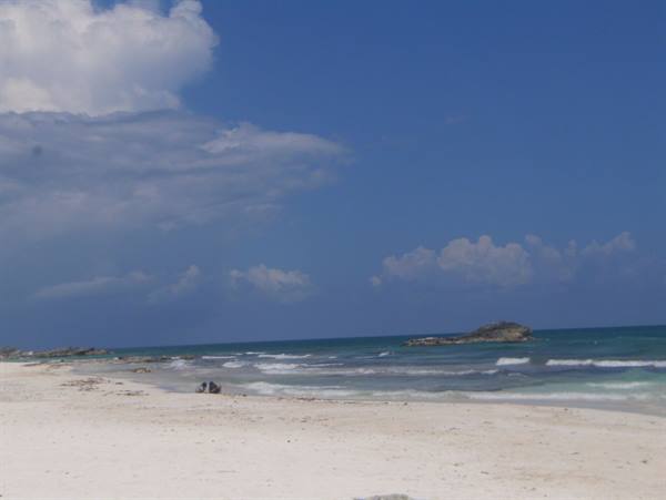 White sand beach with waves and rocky reef under cloudy sky