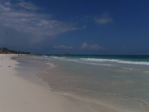 White sand beach with turquoise waves and few swimmers under a cloudy sky