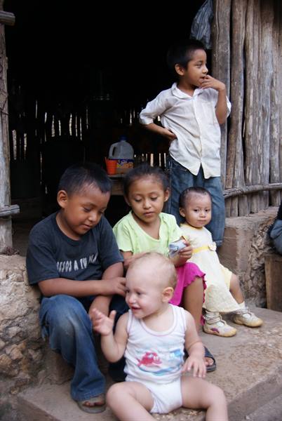 Five children sitting on stone steps outside a wooden house