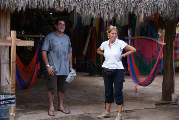 Tourists under thatched roof with colorful hammocks hanging