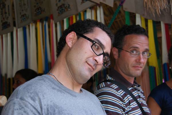 Two men wearing glasses smiling among colorful hanging fabric strips