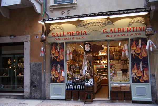 Albertini deli in Verona, lit storefront with cured meats and wine bottles