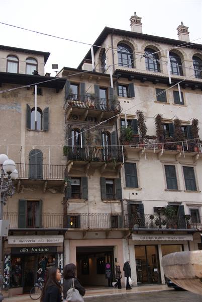 Old buildings with balconies and green shutters over a busy Verona square
