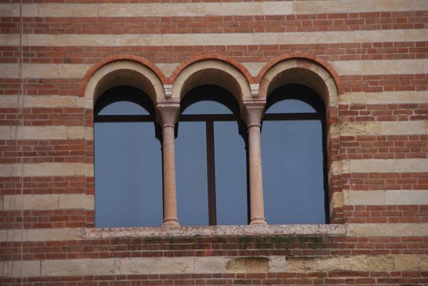 Triple-arched mullioned window with stone columns on striped brick wall
