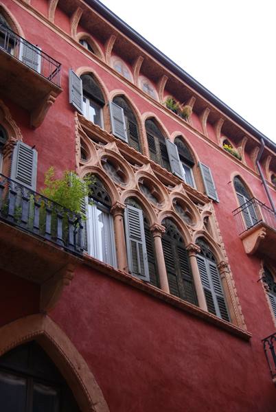 Red Gothic palace facade with pale stone mullioned windows and shutters