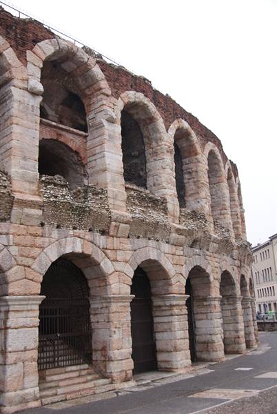 Pink stone walls with Roman arches of Verona Arena under gray sky