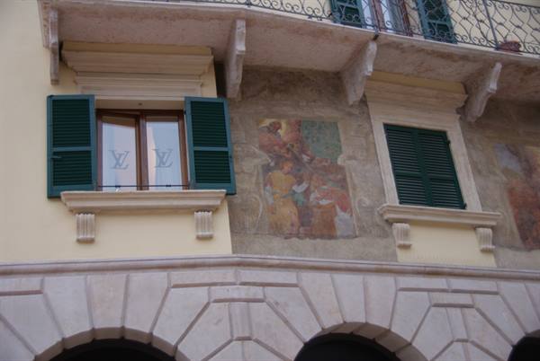 Facade with faded frescoes, green shutters and light stone arches