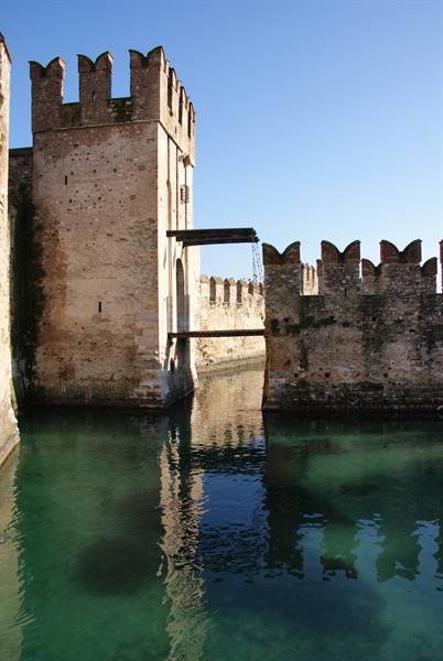 Crenellated towers of Scaligero Castle in Sirmione reflected in turquoise water