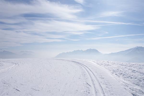Snowy ski slope with tracks, mountains fading into mist