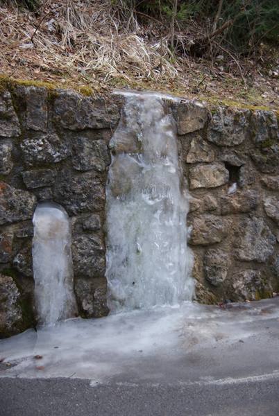 Frozen water cascading over a dry stone wall, icy asphalt below