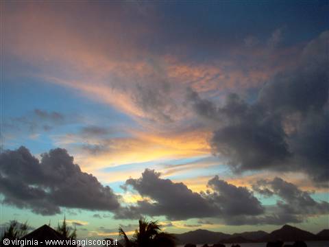 Orange and violet clouds at dusk over dark palm silhouettes and mountains