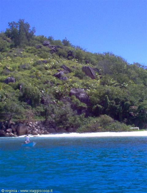 Blue boat on turquoise water in front of tropical hillside with granite boulders