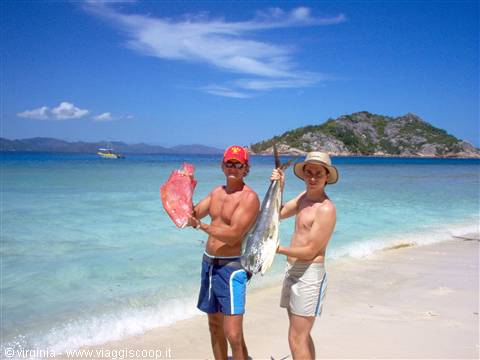 Two men on the beach showing freshly caught fish, rocky islet behind