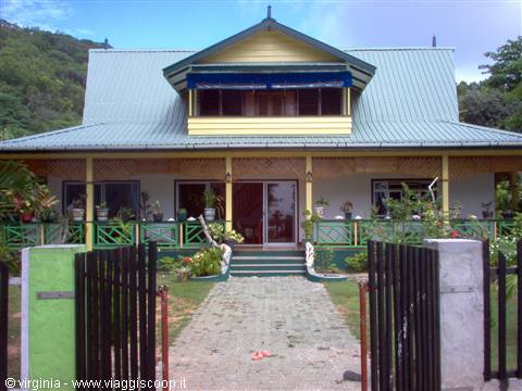 Yellow and green wooden colonial house with tin roof, flowered veranda and open gate