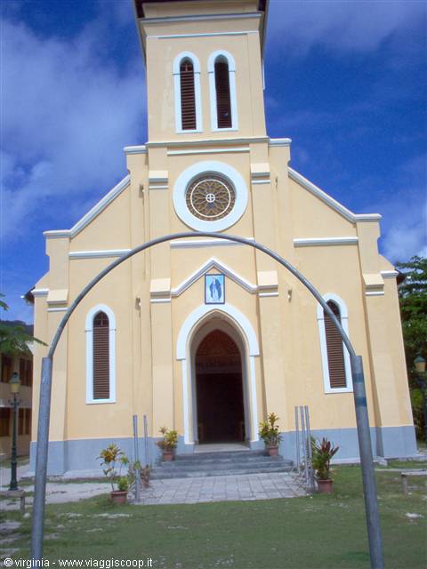 Yellow church with rose window and bell tower, metal arch by entrance