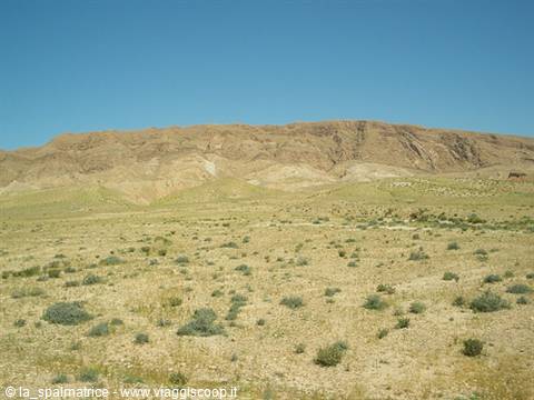Arid rocky mountain above a desert valley with scattered shrubs, clear blue sky