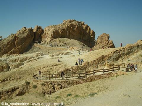 Tourists walking on wooden-fenced path among desert rocks