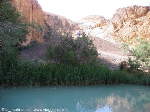 Turquoise pool among ochre rocks and reeds, hikers on the trail