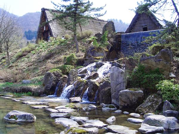 Waterfall over mossy rocks beneath thatched-roof farmhouses in Shirakawa-go