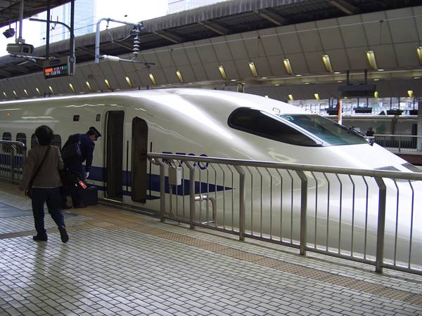 White Shinkansen bullet train at the station, staff with luggage by the door