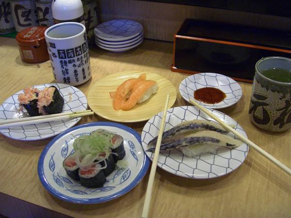 Sushi plates on wooden counter with tea cups and chopsticks