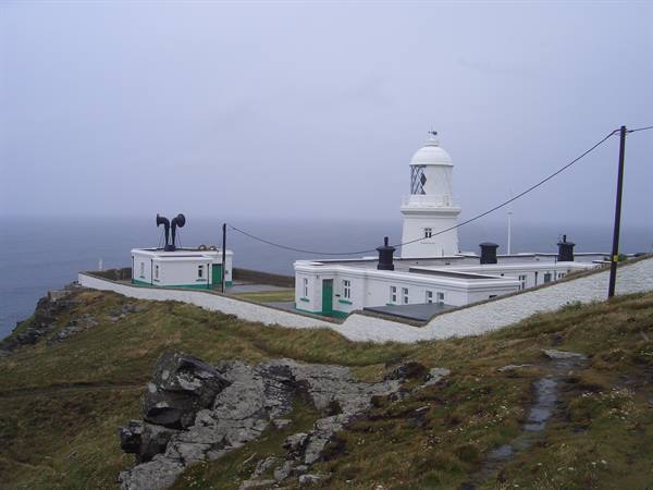 White lighthouse with foghorn on grassy cliff under grey sky, Pendeen