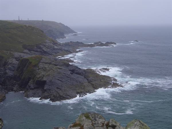 Granite cliffs pounded by waves under fog, mine chimneys on the headland, Cornwall
