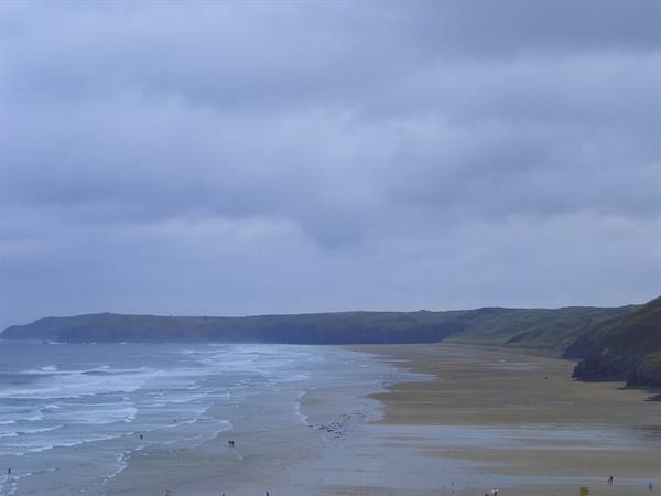 Watergate Bay: wet sandy beach, rolling waves and green cliffs under cloudy sky