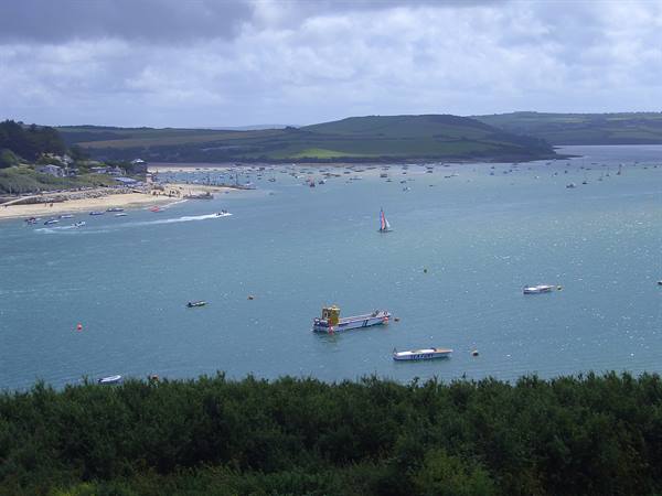 Ferry and sailboats on the estuary, sandy beach and green hills under clouds