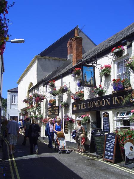 Pedestrians outside the London Inn, white pub with hanging flowers and black sign, blue sky