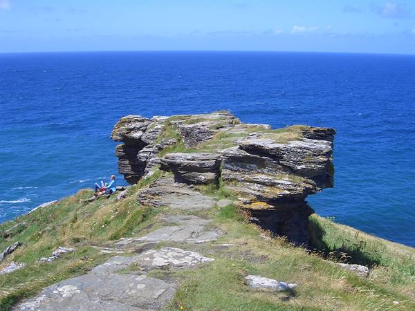 Tourist sitting on grassy slate rocks above the blue sea, Tintagel