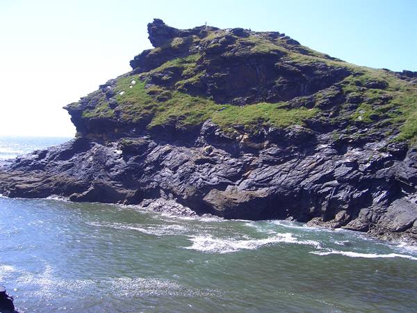 Dark grassy rock cliffs plunge into the sea beneath a clear blue sky