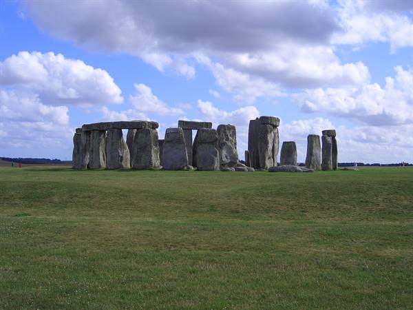 Stonehenge's megalithic stones on green grass beneath white clouds