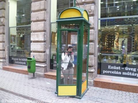 Green and yellow phone booth, photographer reflected in the glass, city shops