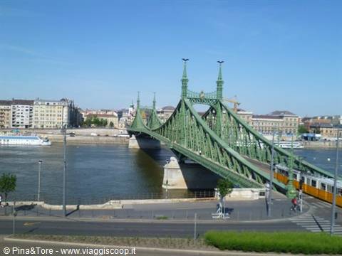 Budapest's green iron Liberty Bridge, a yellow tram crosses the Danube under blue sky